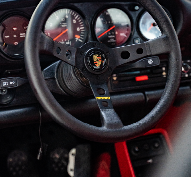 تفصيل داخلي لبورشه – تنظيف دقيق وفخامة مخصصة للسائق صورة مقربة لعجلة قيادة MOMO في بورشه ولوحة العدادات بعد خدمة تنظيف داخلي احترافي